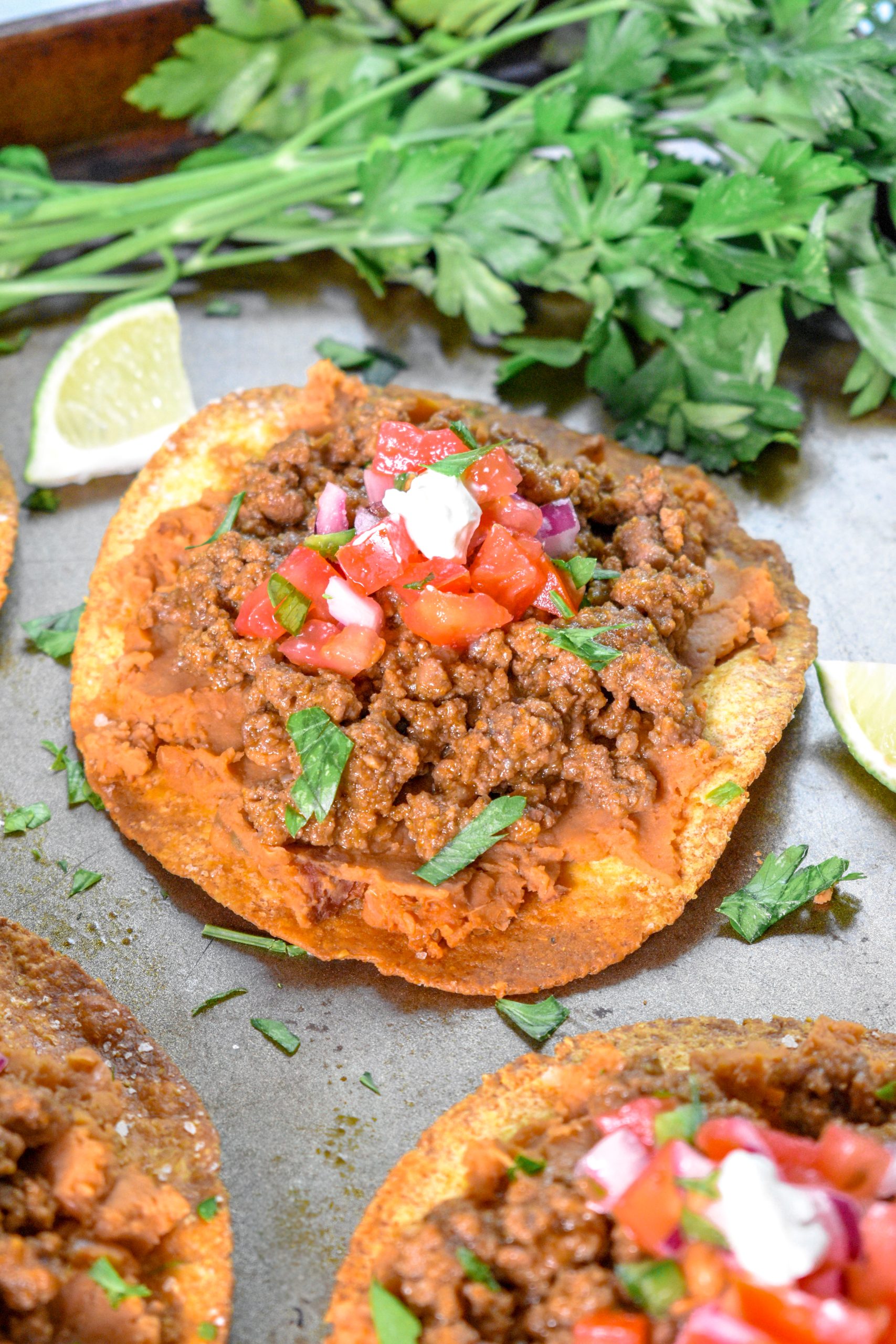This is an image of beef and been tostadas on a sheet pan topped with pico de gallo and crema