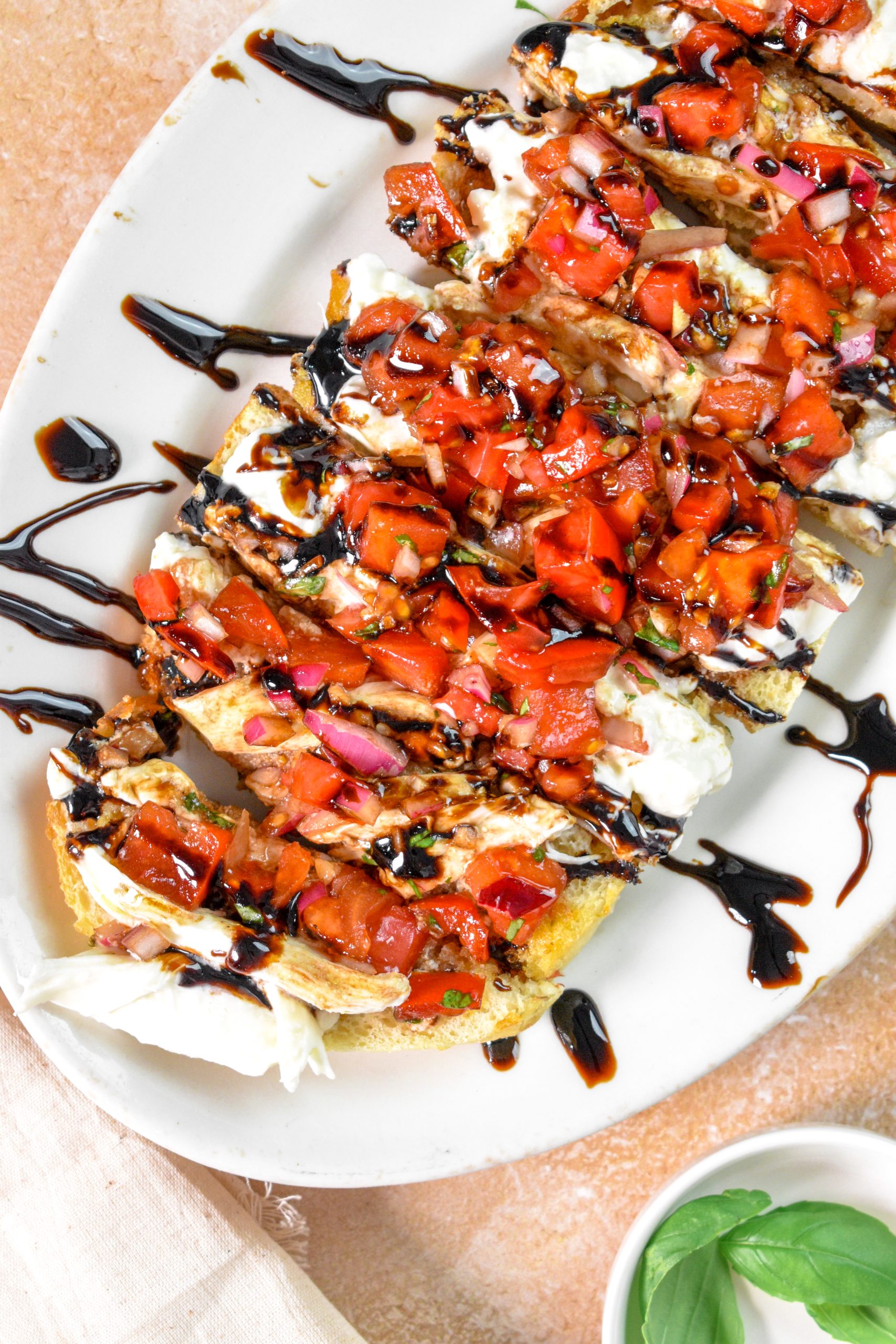 This is an image of bruschetta and burrata on toasted garlic bread sitting on a white plate with basil on the side