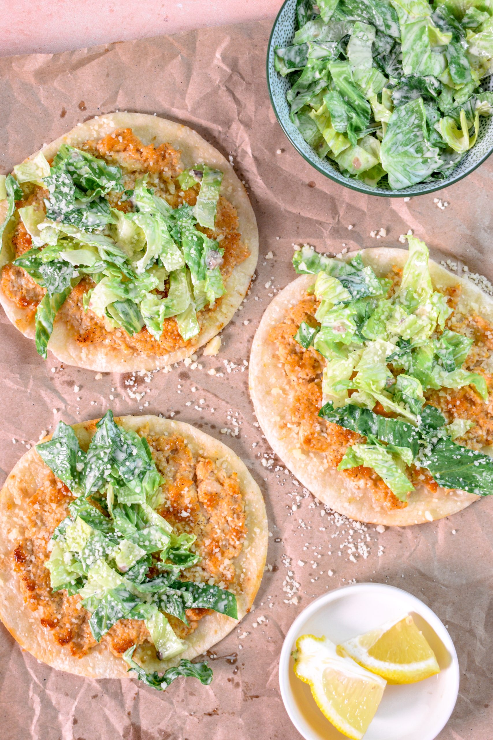 This is an image of 3 chicken caesar smash tacos with lemons and caesar salad on the side