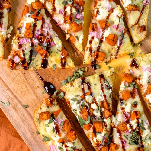 This is an image of slices of Sweet Potato and Goat Cheese Fall Flatbread sitting on a wood cutting board