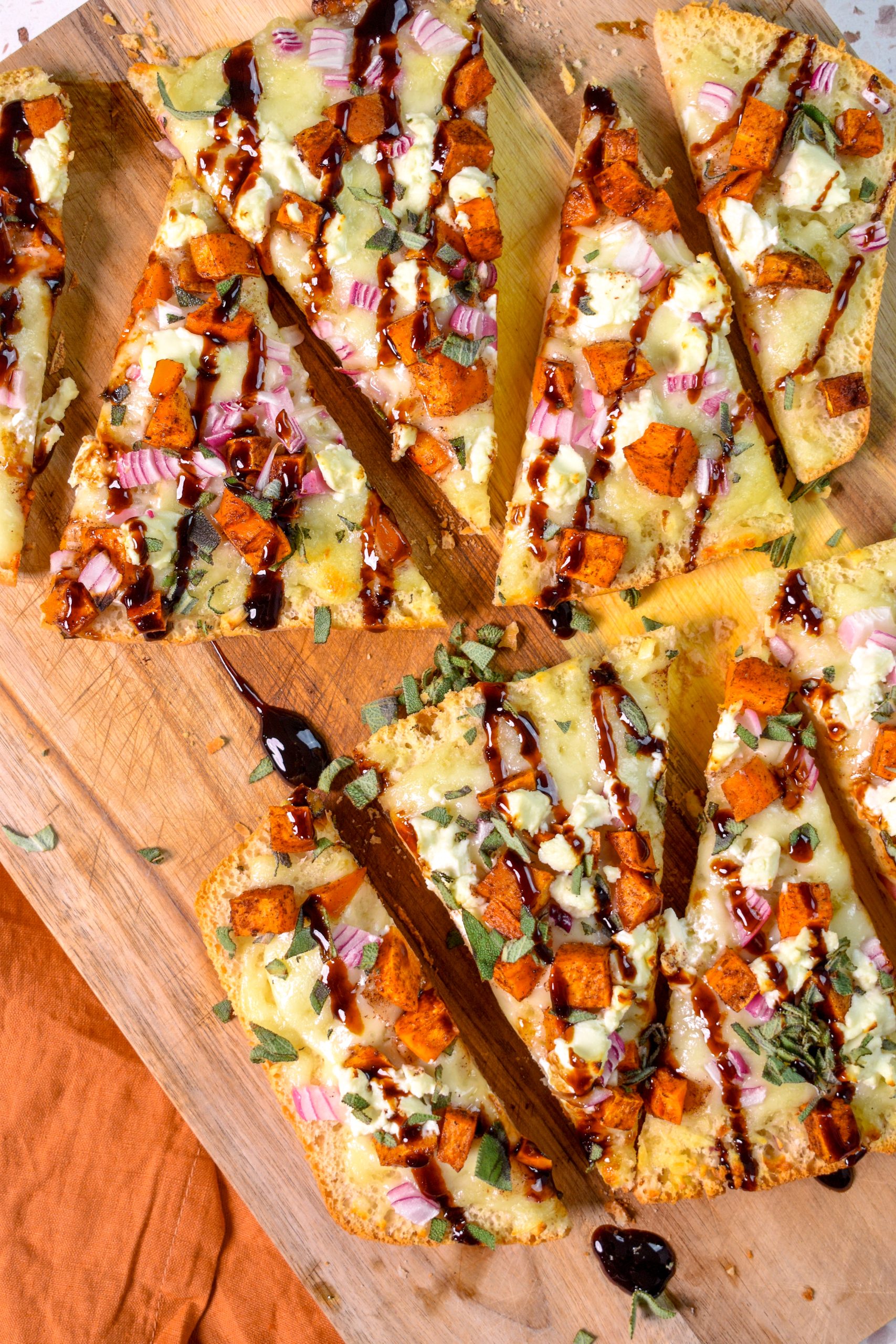This is an image of slices of Sweet Potato and Goat Cheese Fall Flatbread sitting on a wood cutting board