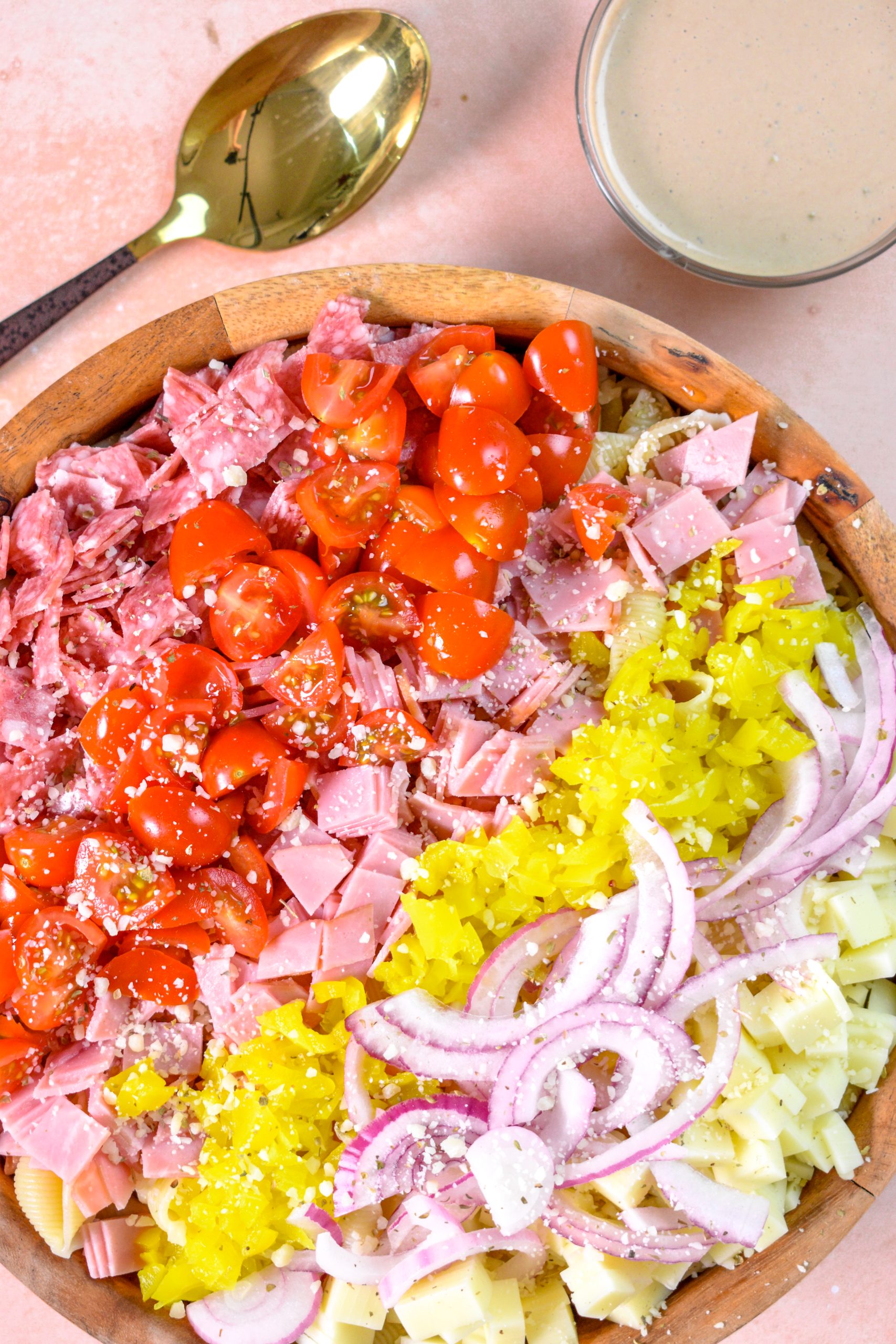This is an image of grinder pasta salad sitting in a wooden bowl with grinder sauce and a spoon on the side