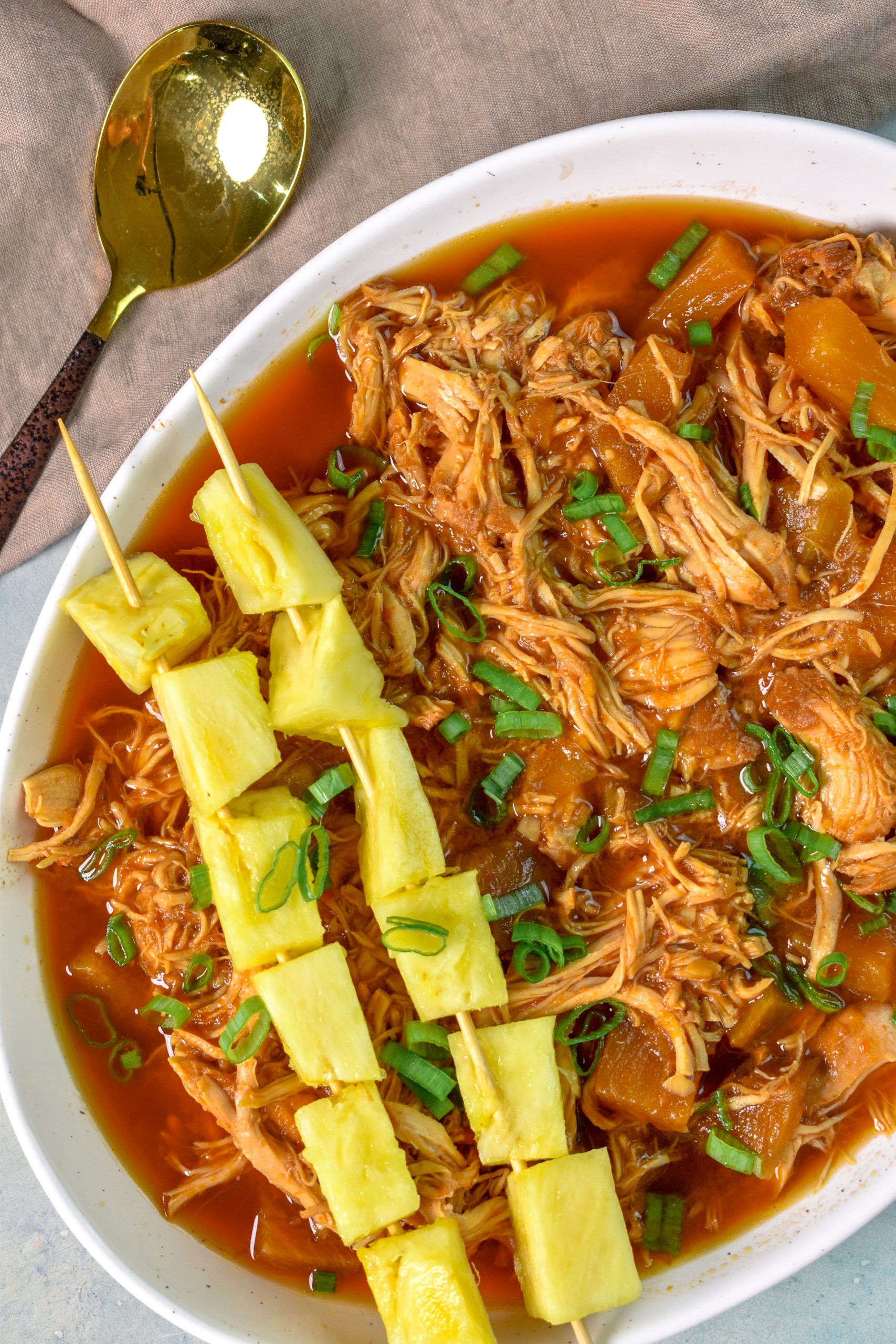This is an image of slow cooker hawaiian chicken sitting in a serving dish with a side of pineapple skewers resting on top