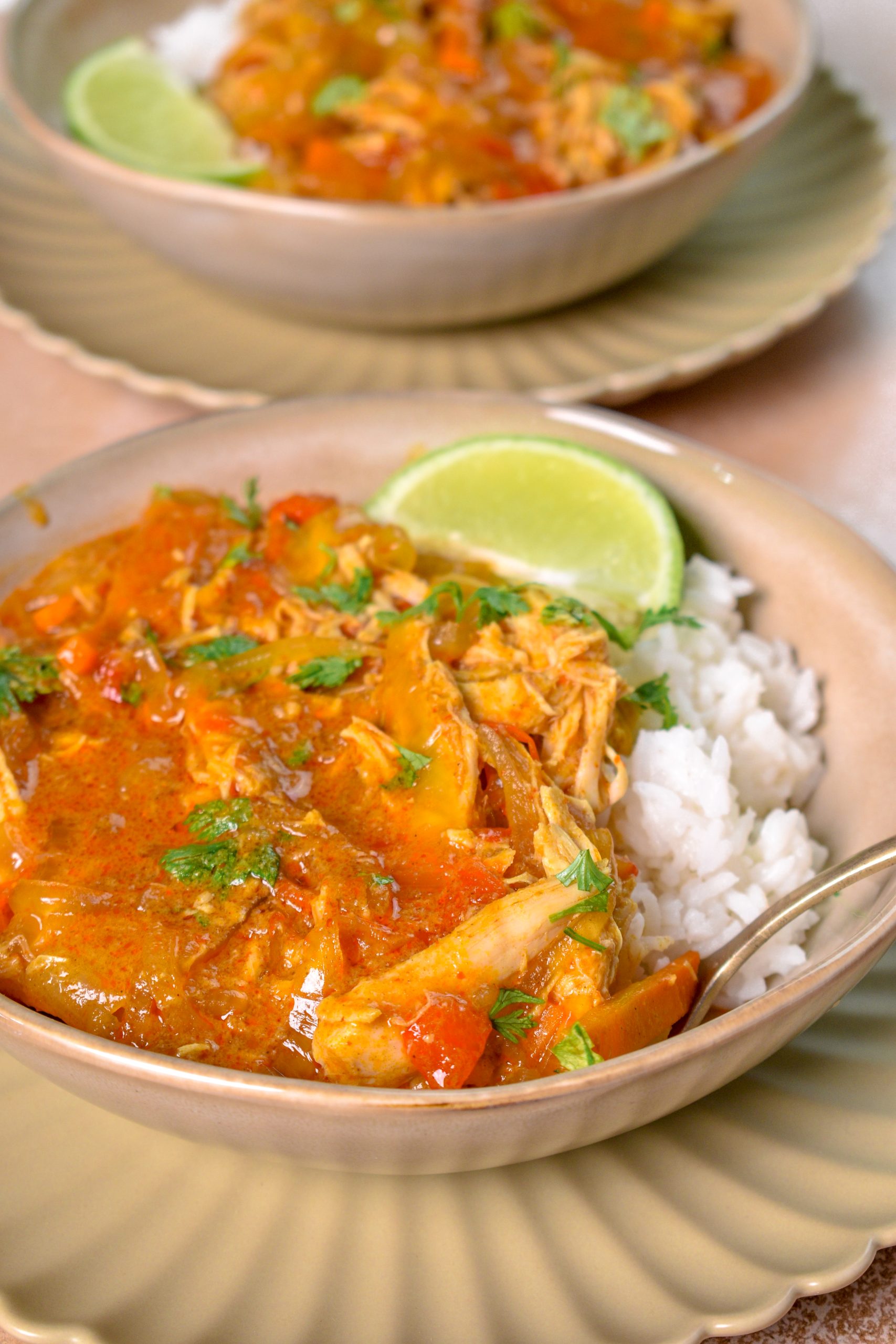 This is an image of slow cooker thai red curry chicken sitting in a bowl over a bed of rice with a lime wedge on the side