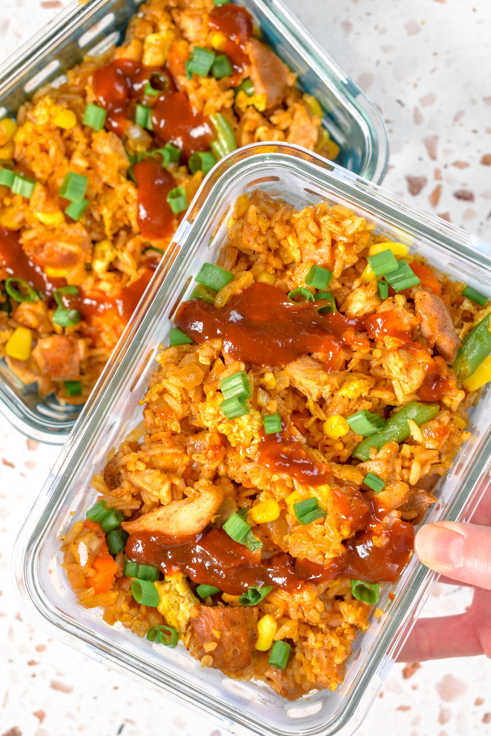 This is a picture of bbq chicken fried rice topped with bbq sauce and scallions. The Fried rice is inside of Tupperware.