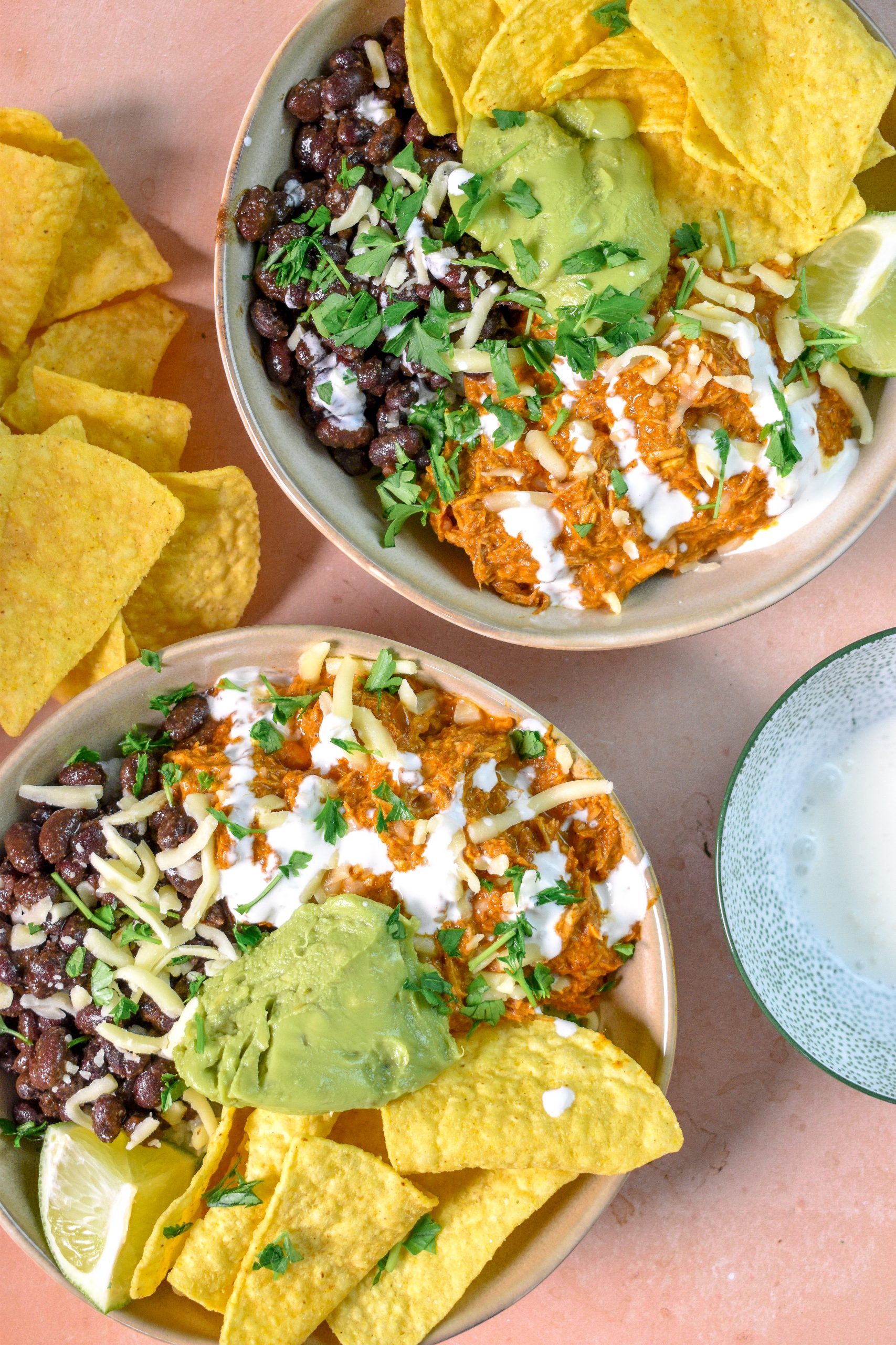 This is an image of slow cooker chicken enchilada bowls with beans, guacamole, rice, and chips, topped with cilantro.