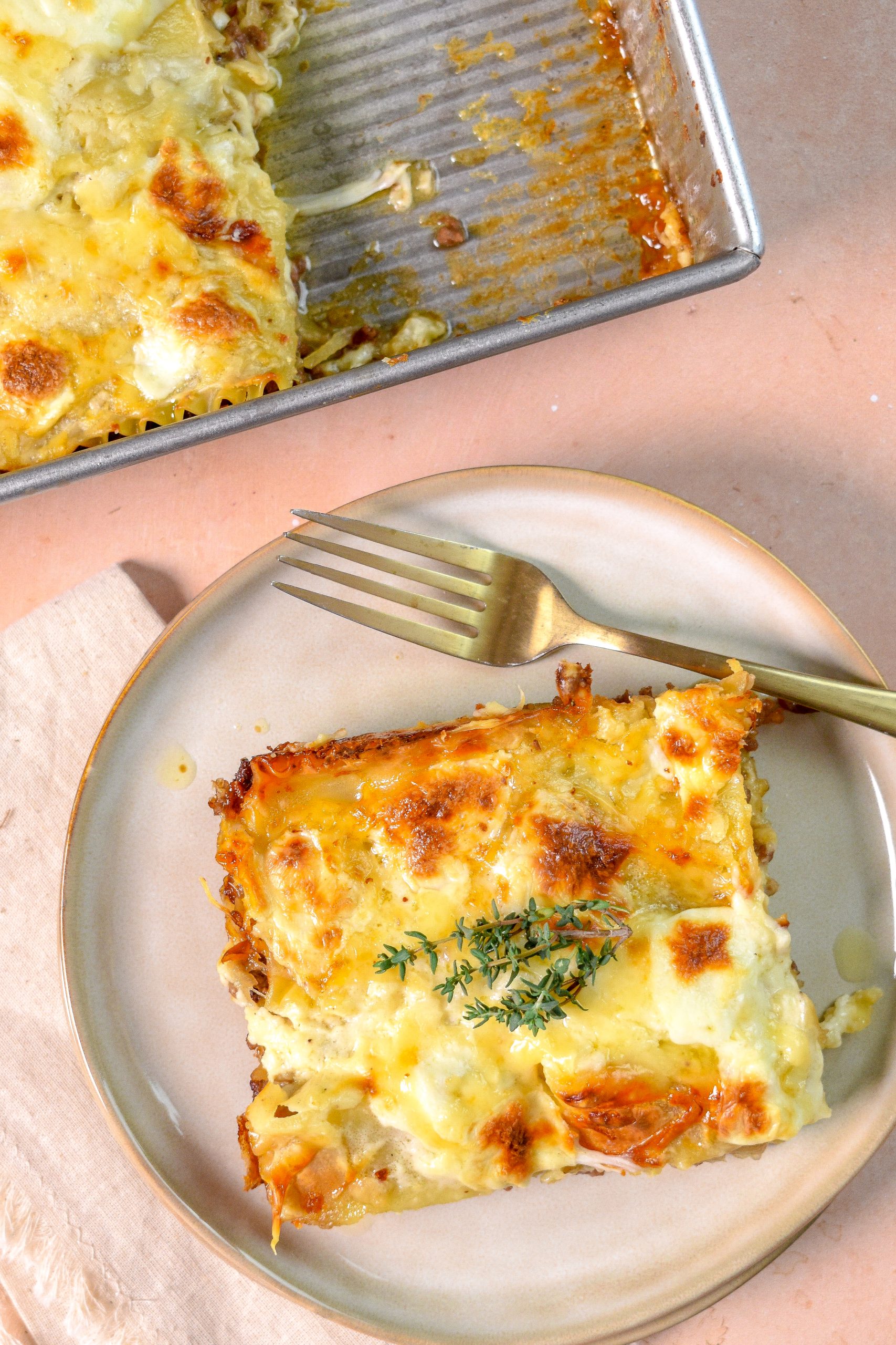 This is an image of french onion lasagna sitting on a tan plate with a fork. In the top of the image is the whole tray of lasagna.