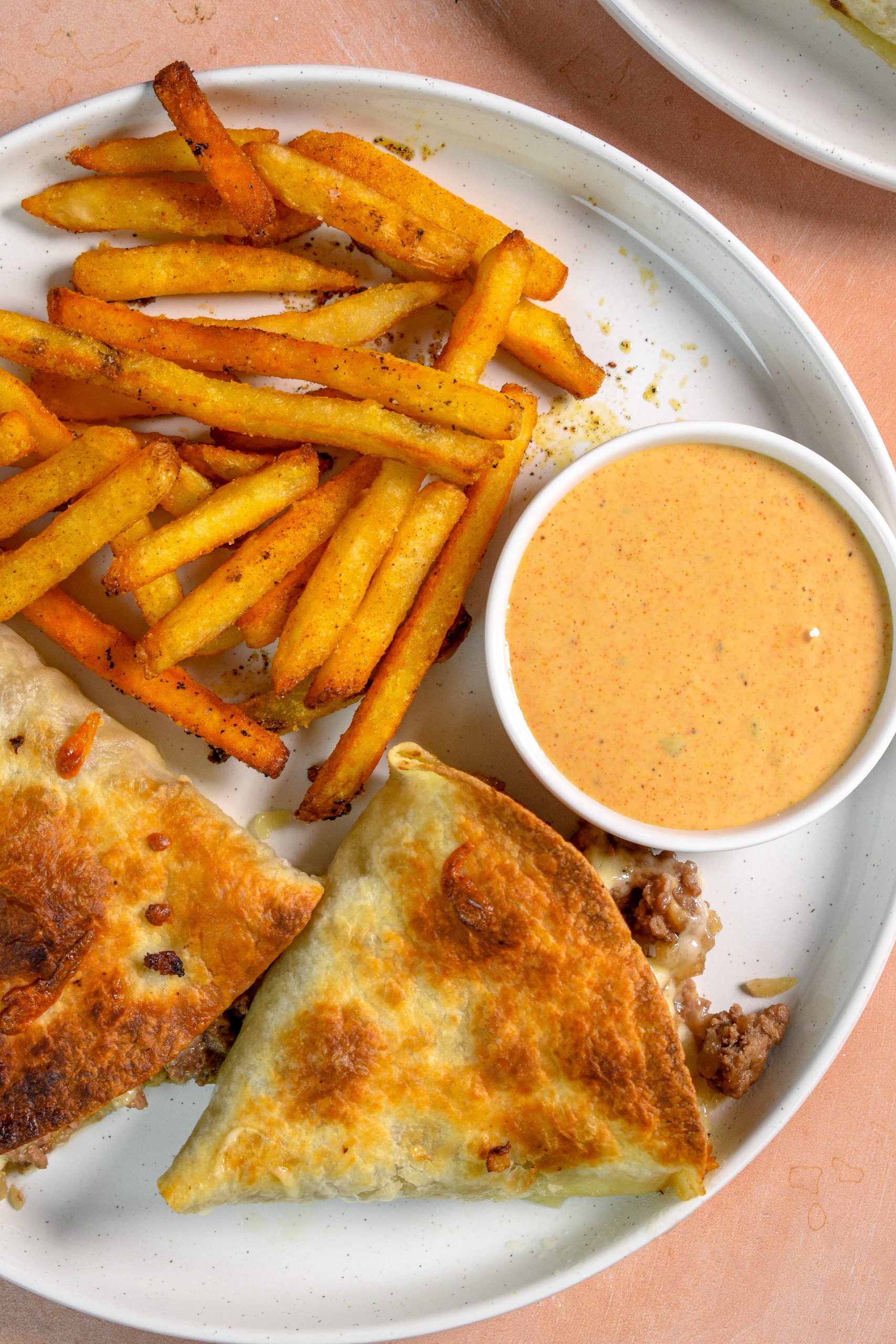 This is an image of tortilla cheeseburger pockets sitting on a white plate with fries and sauce on the side.