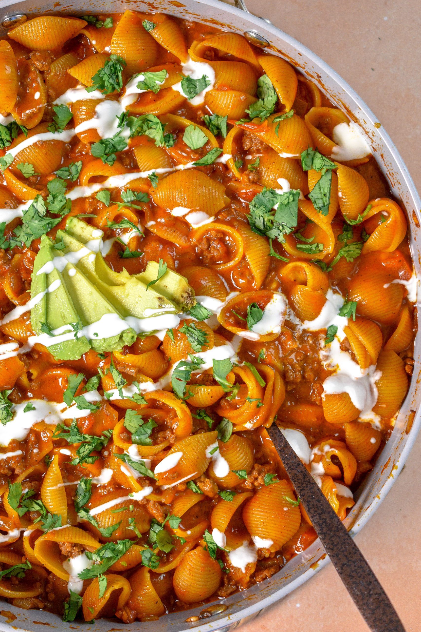 This is a pan of one pot beef enchilada pasta topped with avocado slices, sour cream, and cilantro.