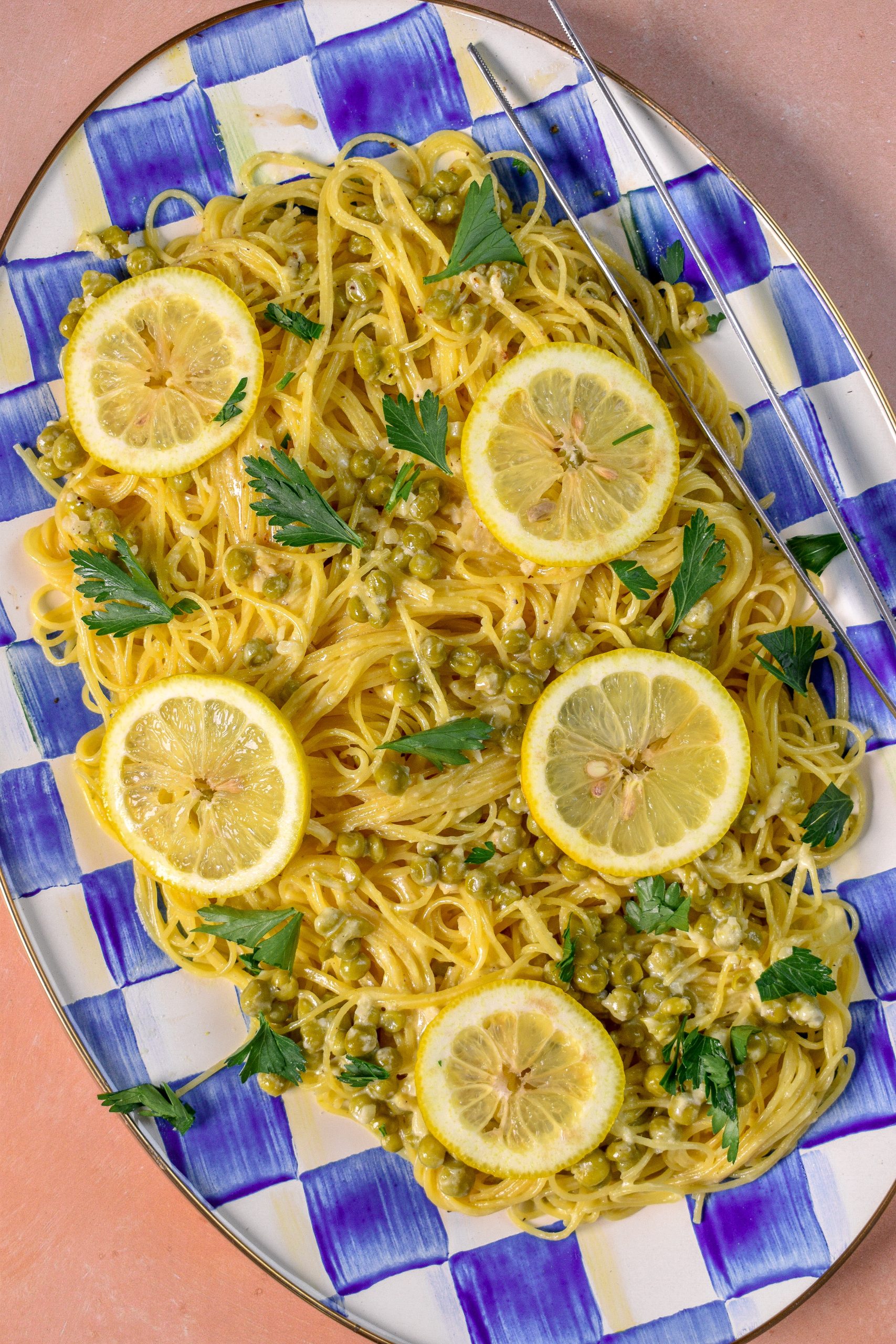 This is an image of creamy lemon garlic pasta sitting on a checkered serving tray with tweezers on the side. The pasta is topped with parsley.